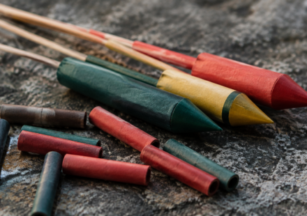 Nezapálené farebné pyrotechnické rakety a papierové tubusy na kamennom podklade – AI ilustrácia.
